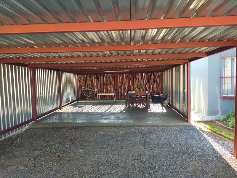 A covered carport or garage area featuring a corrugated metal roof and wall cladding with a concrete base and gravel driveway.