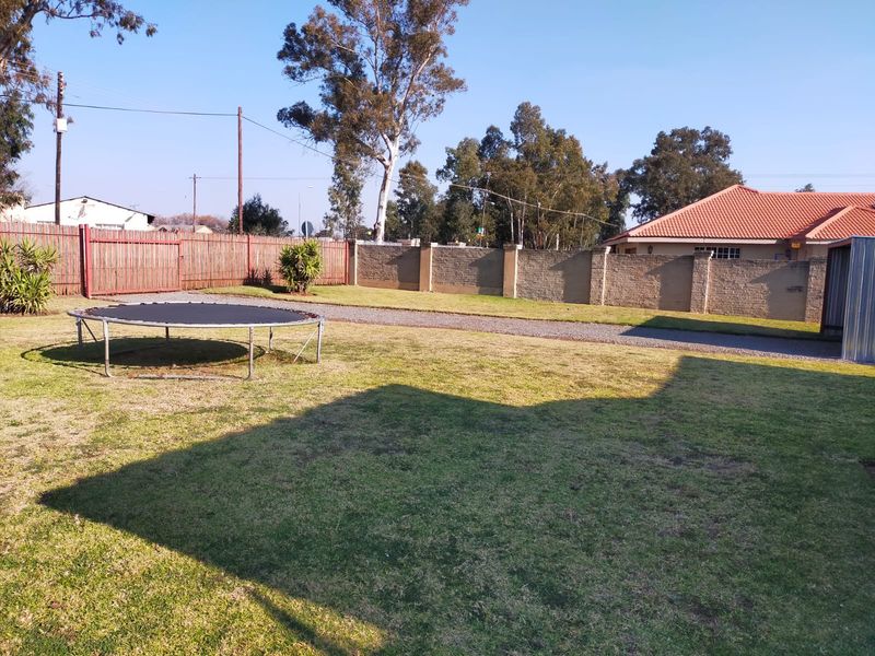 A spacious backyard featuring a well-maintained lawn, gravel driveway, and secure perimeter walling with timber fencing.