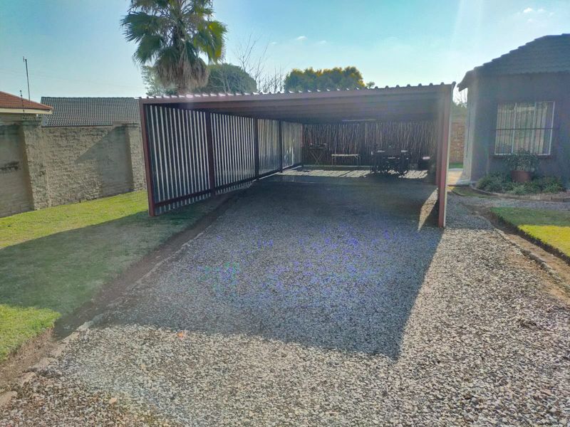 A functional metal carport structure providing covered parking, situated on a gravel driveway adjacent to the main house.