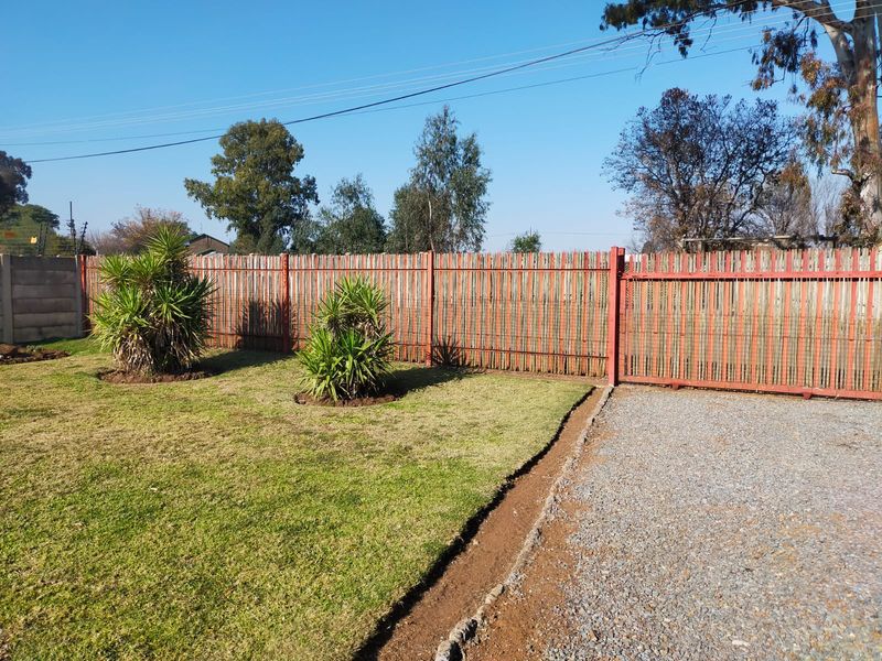 Front exterior view featuring a gravel driveway, maintained lawn, and timber slat boundary fencing with a metal gate.
