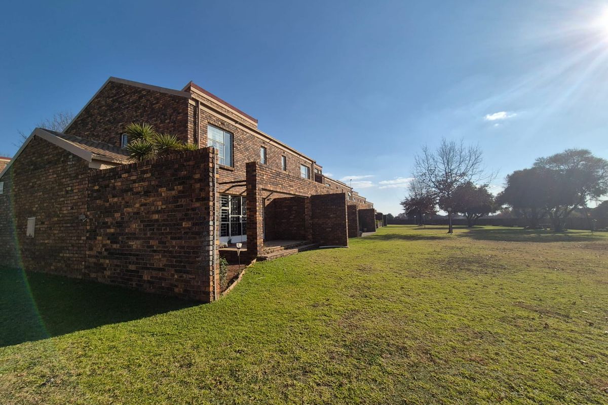Rear view of a face-brick townhouse complex featuring private patio areas and access to a spacious communal garden.