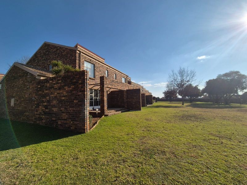 Rear view of a face-brick townhouse complex featuring private patio areas and access to a spacious communal garden.
