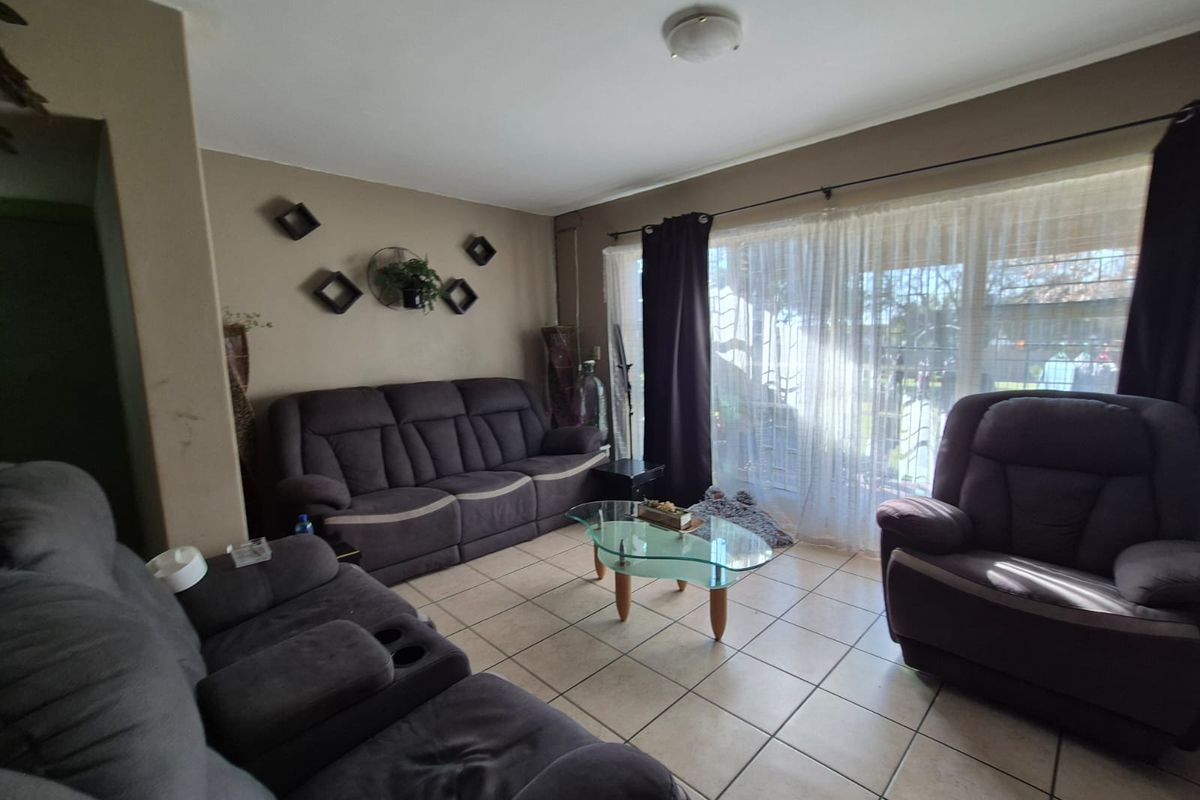 A comfortable living room featuring ceramic floor tiles and a large sliding glass door with security gate, providing access to the outdoor area.