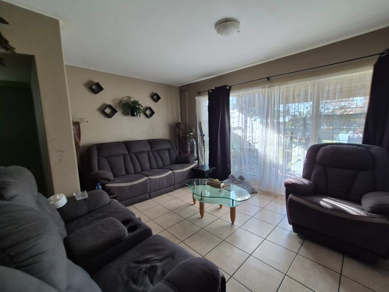 A comfortable living room featuring ceramic floor tiles and a large sliding glass door with security gate, providing access to the outdoor area.