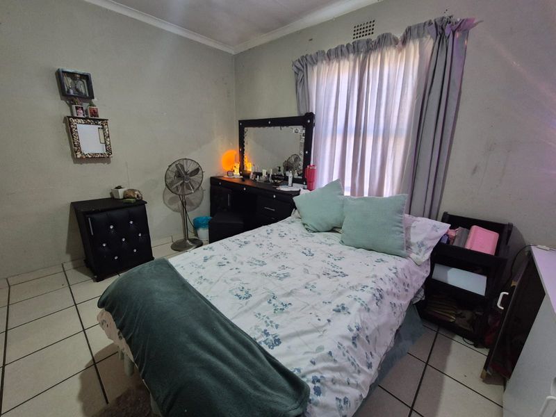 A bedroom featuring tiled flooring and a window with curtain rails. The room requires cosmetic updates to the wall finishes.