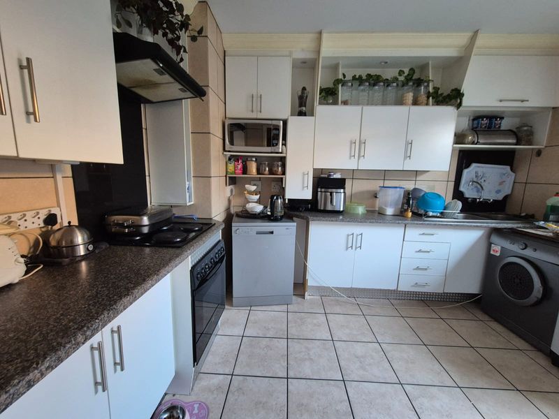 Functional kitchen featuring white cabinetry, laminate countertops, tiled backsplash, and integrated appliances, offering a practical layout with potential for modern cosmetic updates.