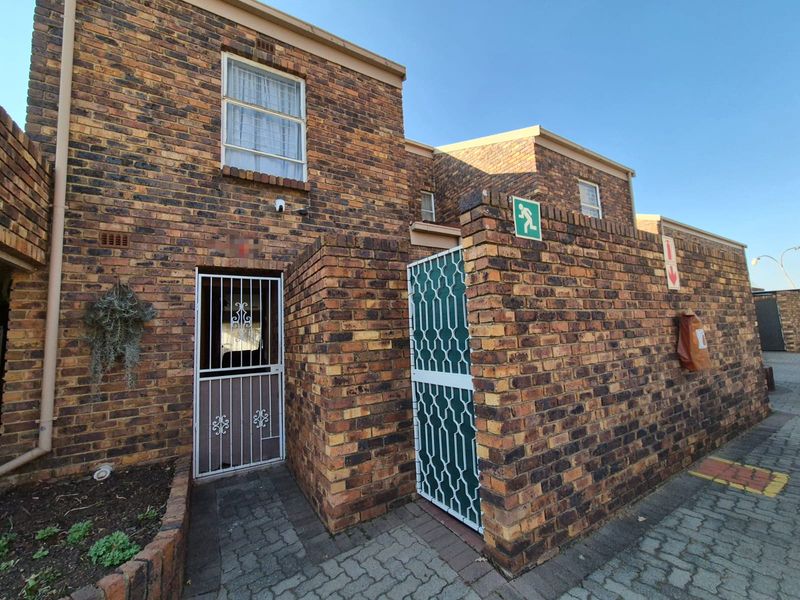 Front exterior view of a face brick townhouse featuring a secure entrance gate, paved walkway, and emergency safety equipment.