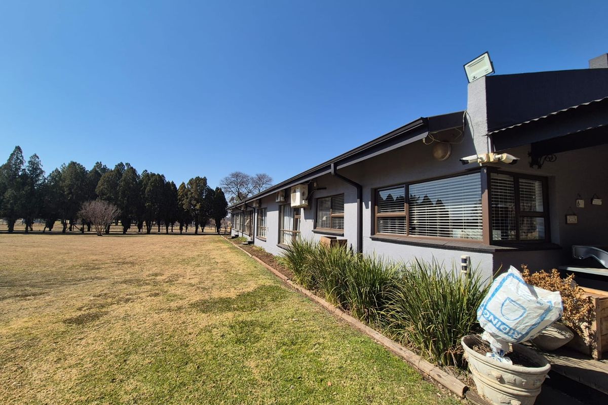 Rear view of the property featuring a long exterior wall, aluminium windows, security fixtures, and a large open garden area.