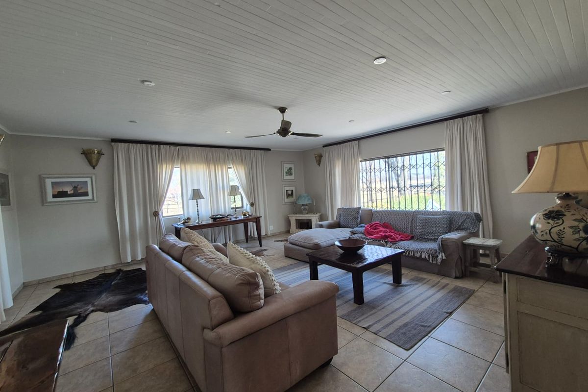 Spacious living room featuring tiled flooring, a tongue and groove ceiling with recessed lighting, and large windows fitted with security bars.