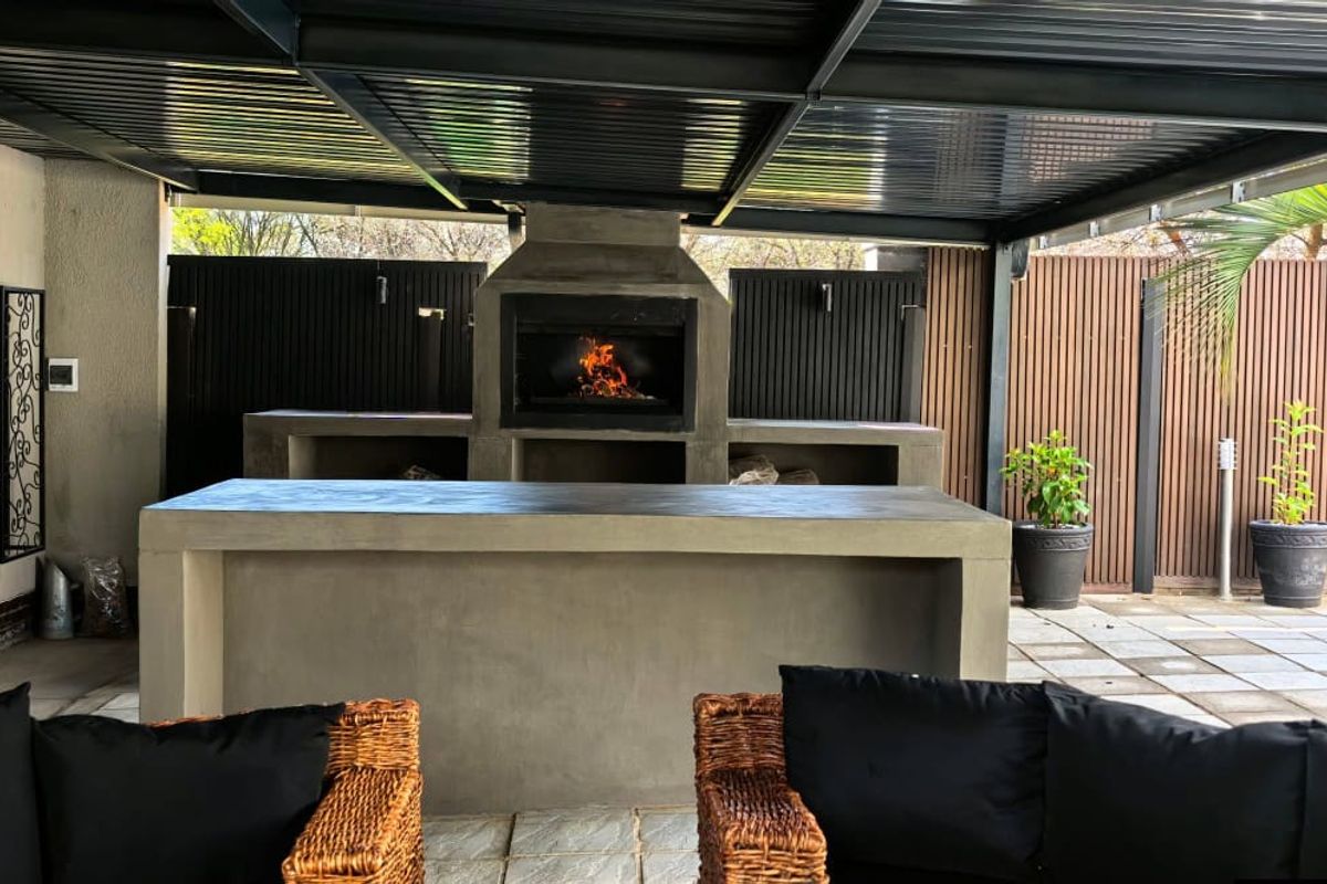 Covered outdoor patio featuring a built-in braai, concrete prep counter, and modern metal roofing, ideal for alfresco dining and entertainment.