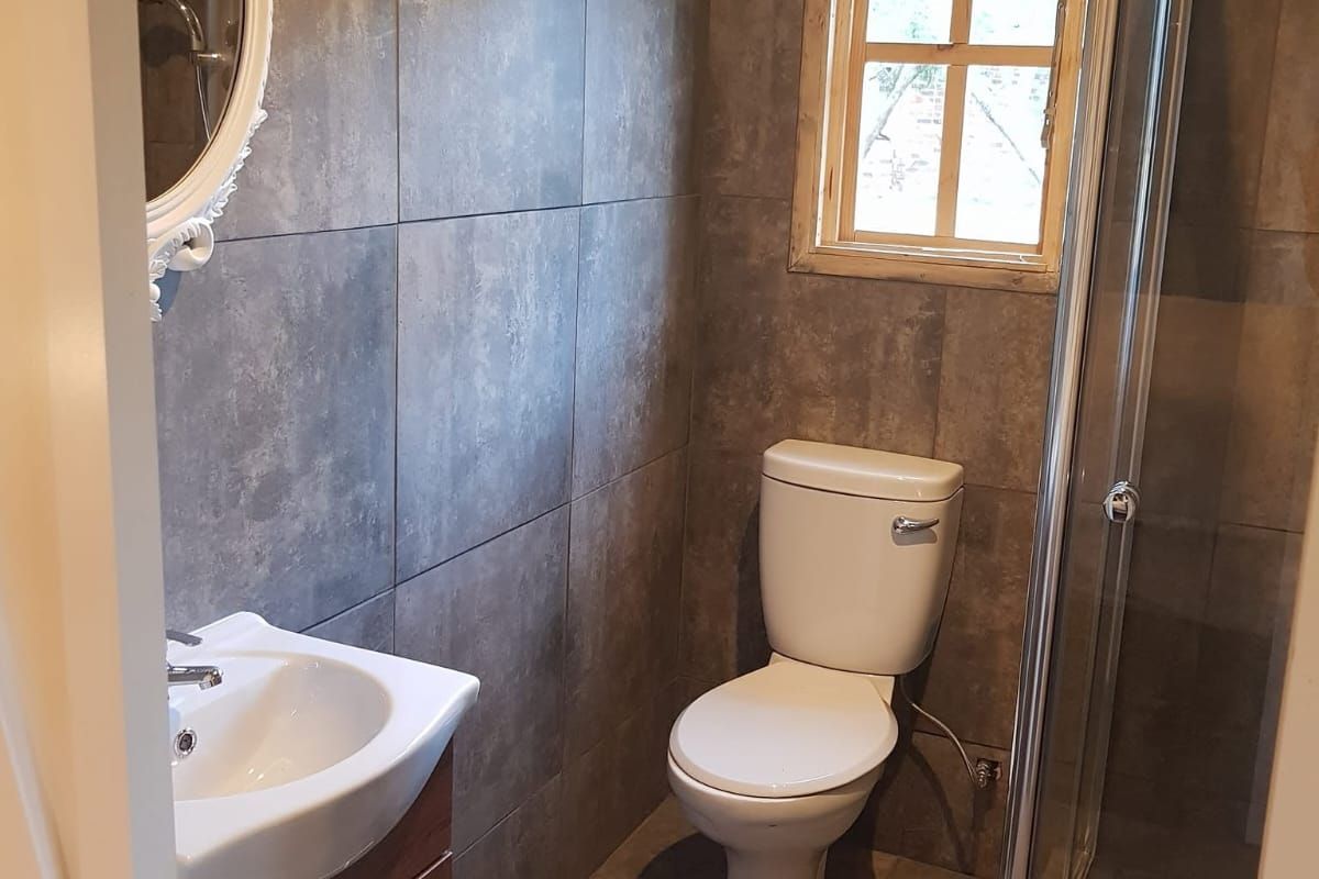 A modern bathroom featuring dark grey wall and floor tiles, a vanity cabinet with basin, a toilet, and a glass-enclosed shower.