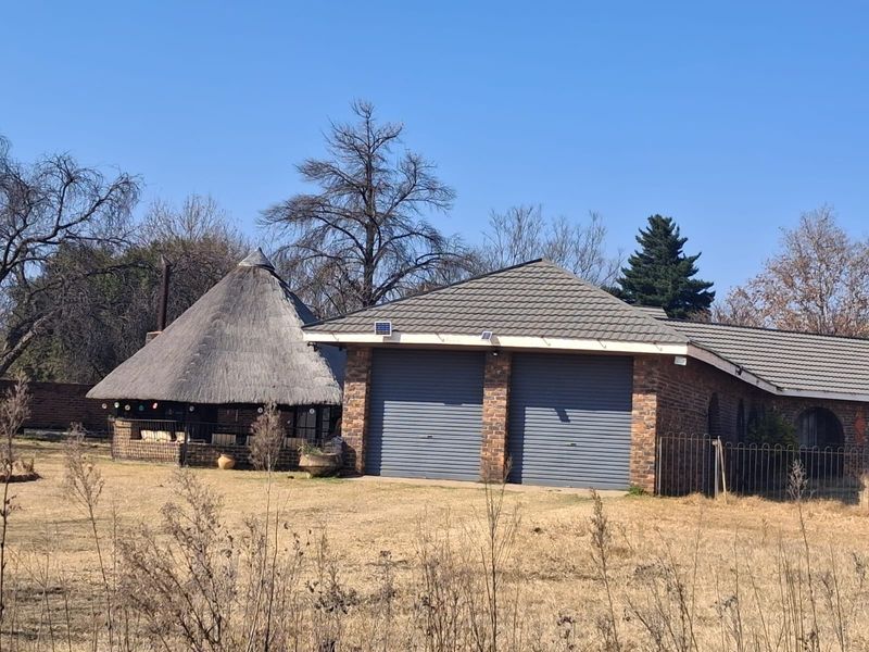 Exterior view of a property featuring a double garage with roller shutter doors and an adjacent thatched lapa structure.