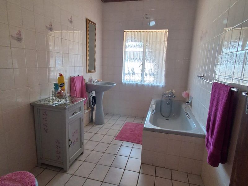 A dated bathroom featuring a pedestal basin, built-in bathtub, fully tiled walls, and a timber tongue and groove ceiling.