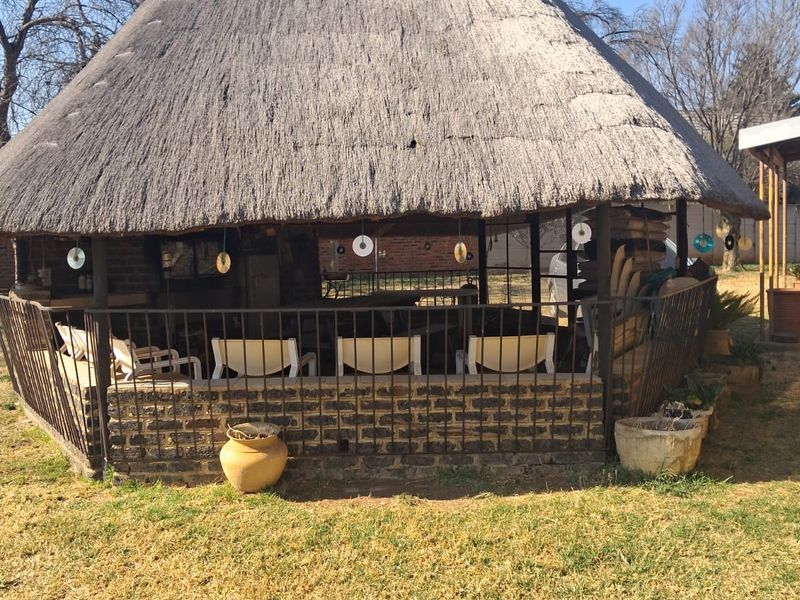 A rustic outdoor entertainment area featuring a traditional thatched roof, brick base, and metal perimeter railing, set within a garden space.