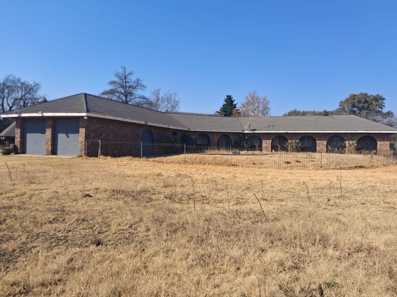 A single-story brick house featuring a tiled roof, double garage with roller doors, and a series of arched window openings set on a large plot.