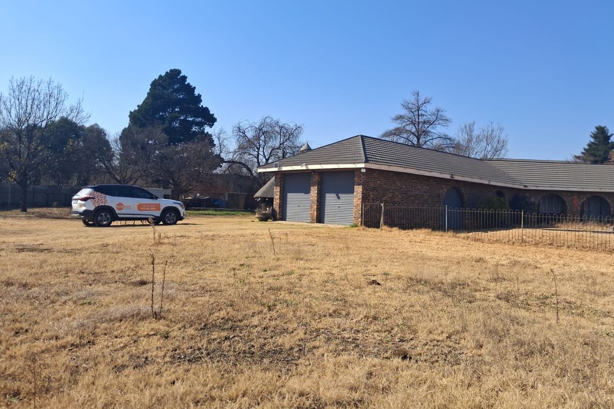 A view of the rear exterior of the property featuring a double garage with brick construction and a tiled roof set on a large plot.