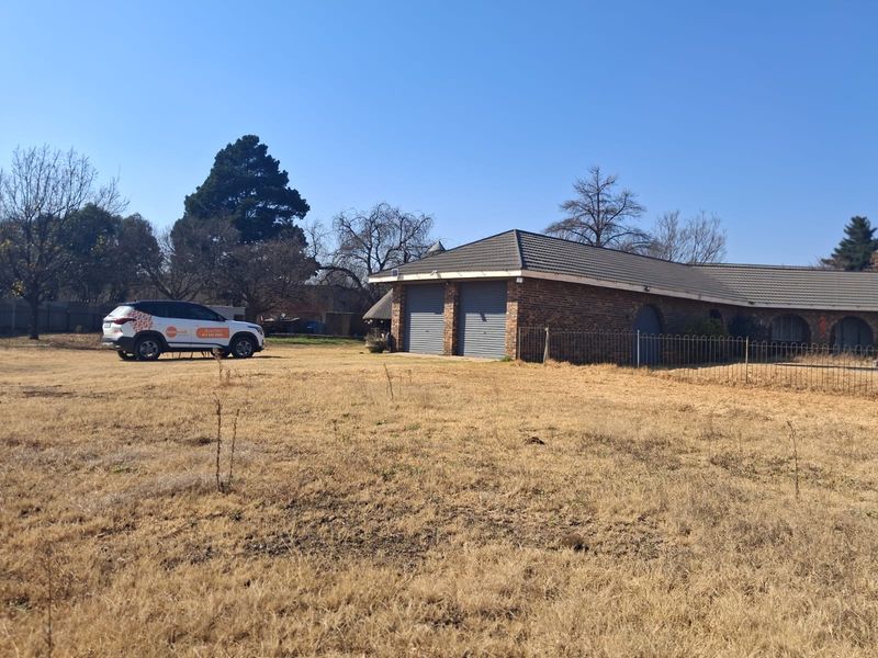 A view of the rear exterior of the property featuring a double garage with brick construction and a tiled roof set on a large plot.
