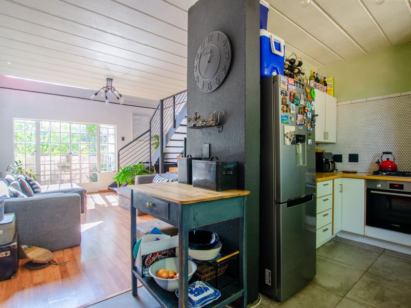 Open-plan living area featuring a kitchen with built-in oven and hob, adjacent to a lounge space with staircase access and sliding door to patio.