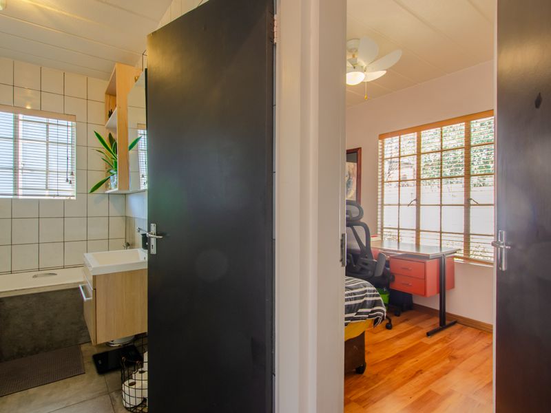 A view from the hallway looking into a tiled bathroom with a vanity and a bedroom featuring laminate flooring and a ceiling fan.