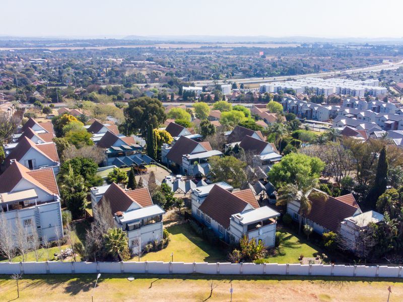 Aerial view of a residential townhouse complex featuring multiple units with pitched tiled roofs, established gardens, and secure perimeter fencing.