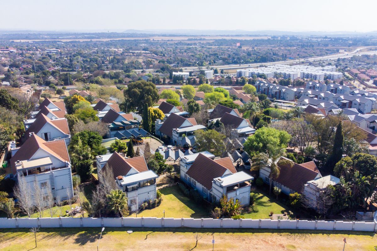 Aerial view of a residential townhouse complex featuring multiple units with pitched tiled roofs, established gardens, and secure perimeter fencing.