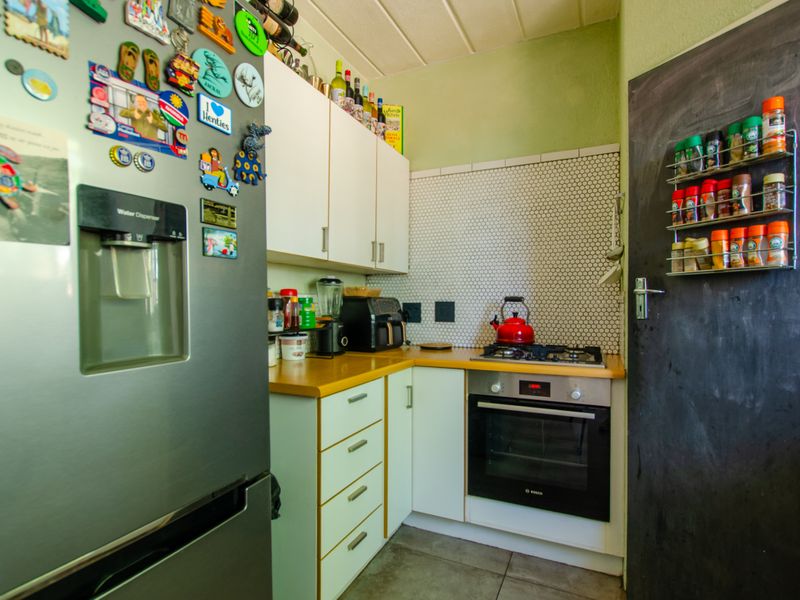 A compact kitchen featuring white cabinetry, laminate countertops, a gas hob, built-in oven, and a distinctive mosaic tile backsplash.