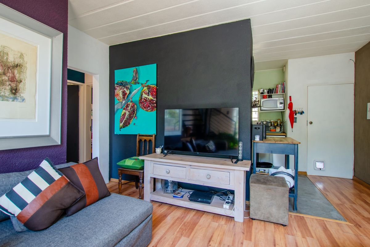 A living room area featuring laminate flooring and a neutral layout, with an adjacent transition space leading to a secondary area.