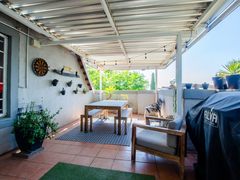 Covered outdoor patio area featuring tiled flooring and a corrugated metal roof structure, providing a functional space for outdoor dining and relaxation.