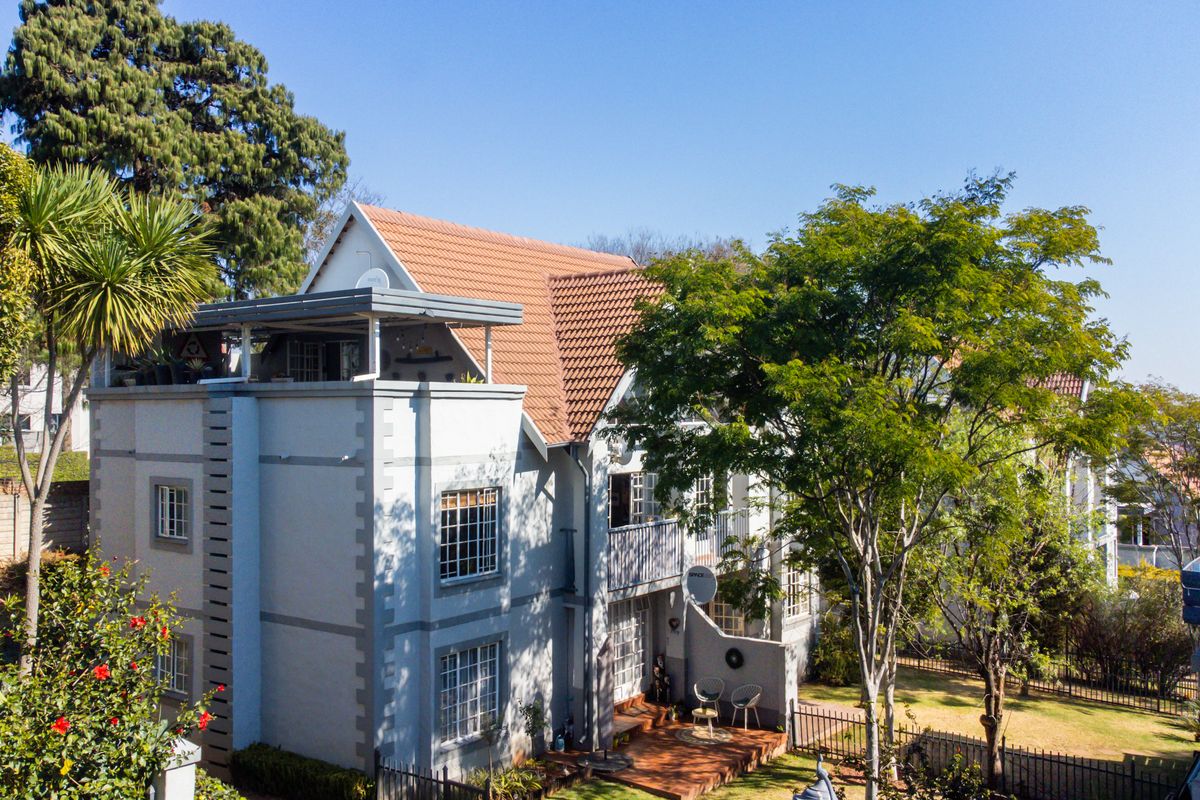 Rear elevation of a multi-story townhouse featuring a tiled roof, a private balcony, and a ground-level timber deck overlooking a landscaped garden.