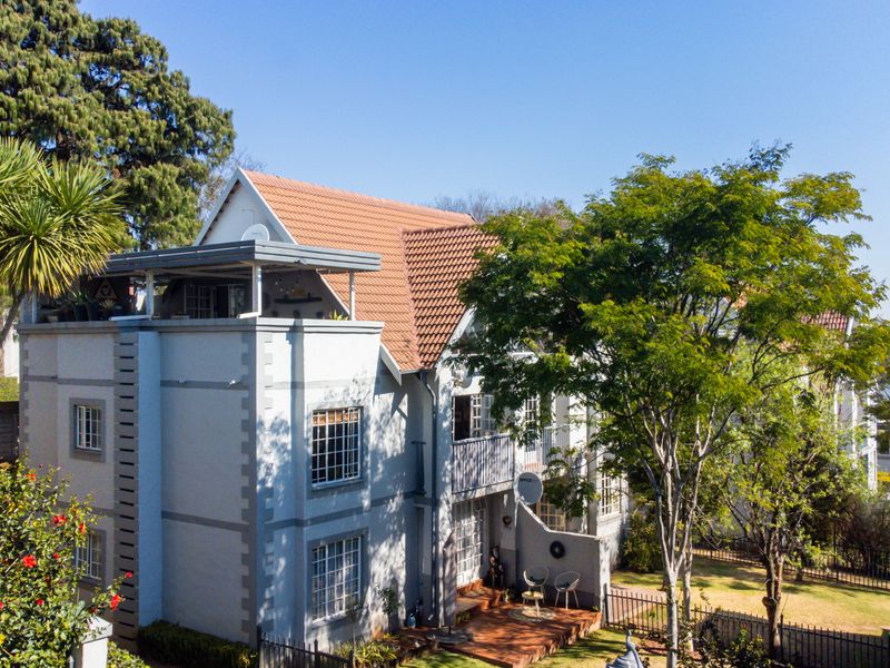 Rear elevation of a multi-story townhouse featuring a tiled roof, a private balcony, and a ground-level timber deck overlooking a landscaped garden.