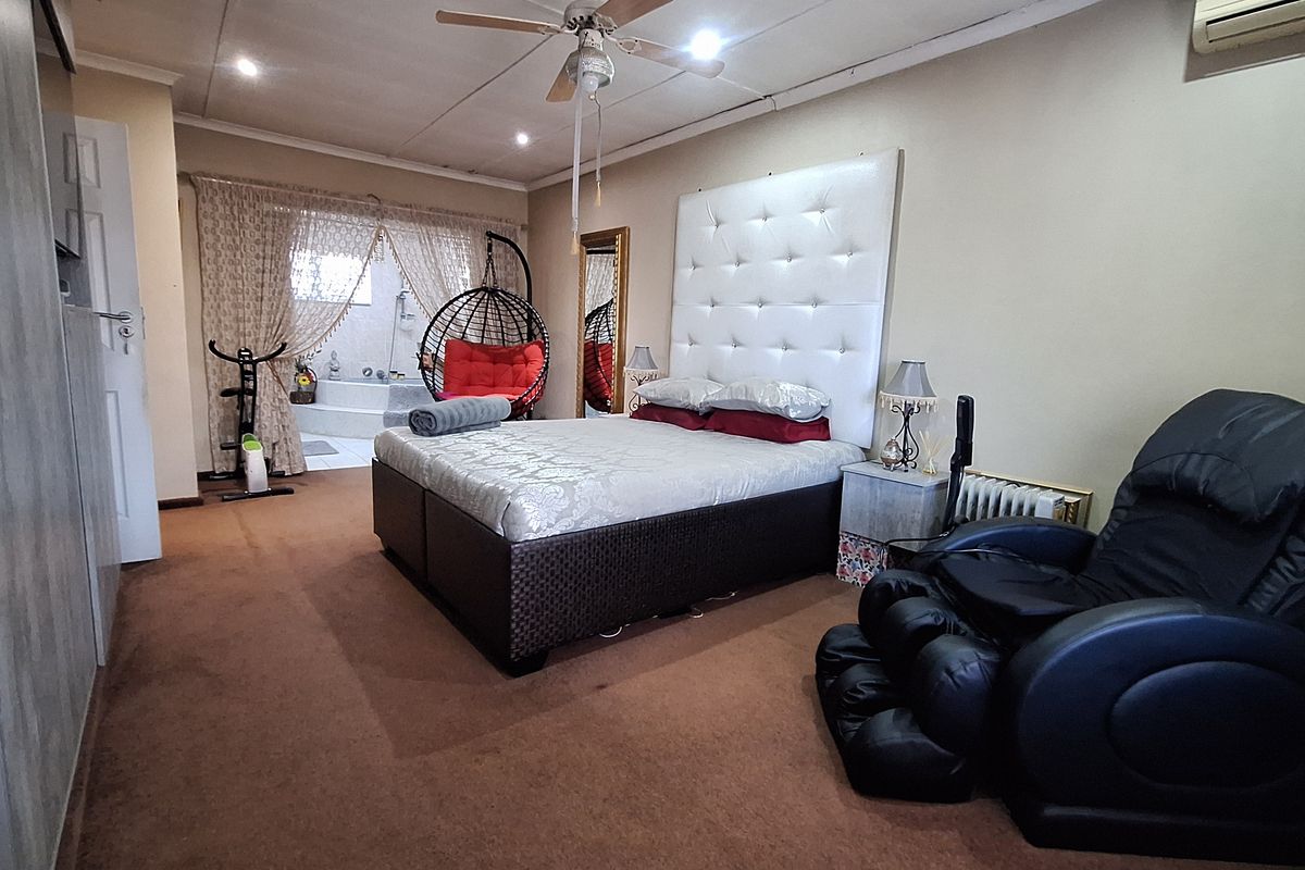 Spacious bedroom featuring a ceiling fan, air conditioning unit, and integrated wardrobe, with an open-plan layout connecting to an adjacent bathroom area.