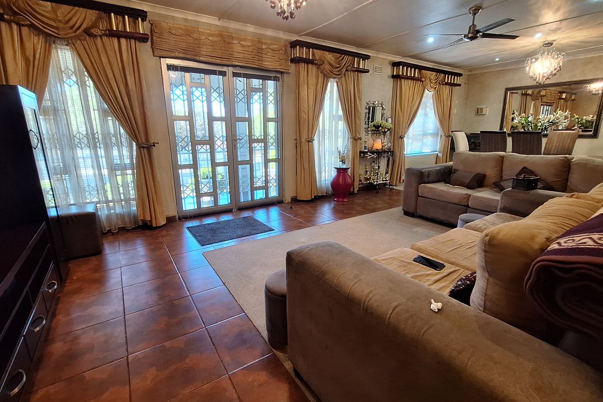 Spacious living room featuring tiled flooring, ceiling fan, decorative chandeliers, and double glass doors with security gates leading to the exterior.
