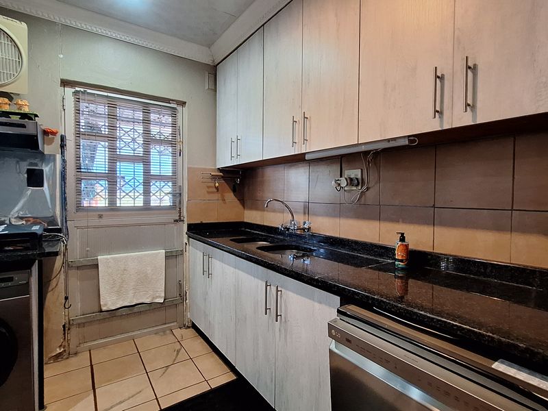 A functional kitchen featuring granite countertops, ample built-in cabinetry, tiled backsplash, and direct access to the exterior via a security-gated door.