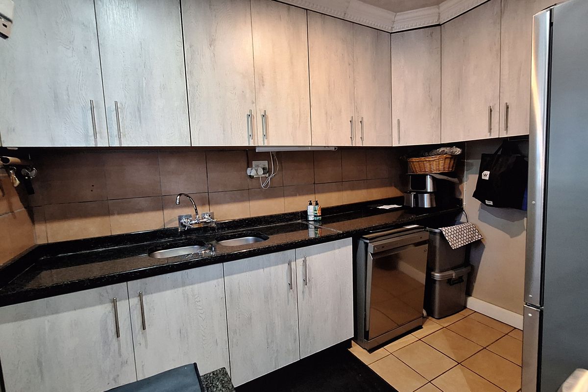 A functional kitchen featuring light wood-grain cabinetry, dark granite countertops, a double basin sink, and tiled backsplash with integrated dishwasher space.