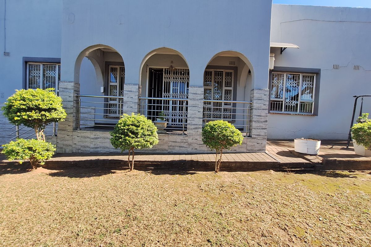 A rear exterior view featuring an arched patio with stone-clad pillars, stainless steel balustrades, and security-fitted windows overlooking a garden area.