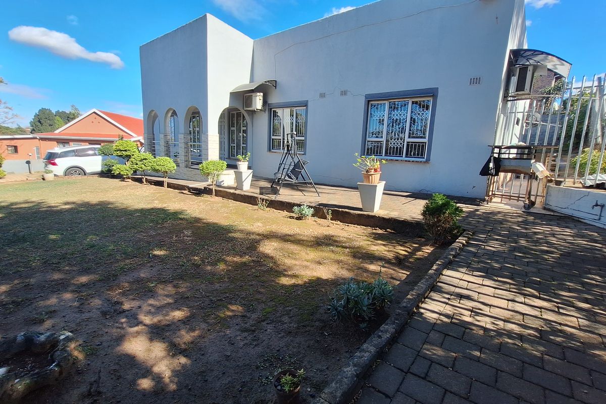Rear view of the house featuring a paved patio area, arched entrance, and security-fitted windows overlooking a garden space.