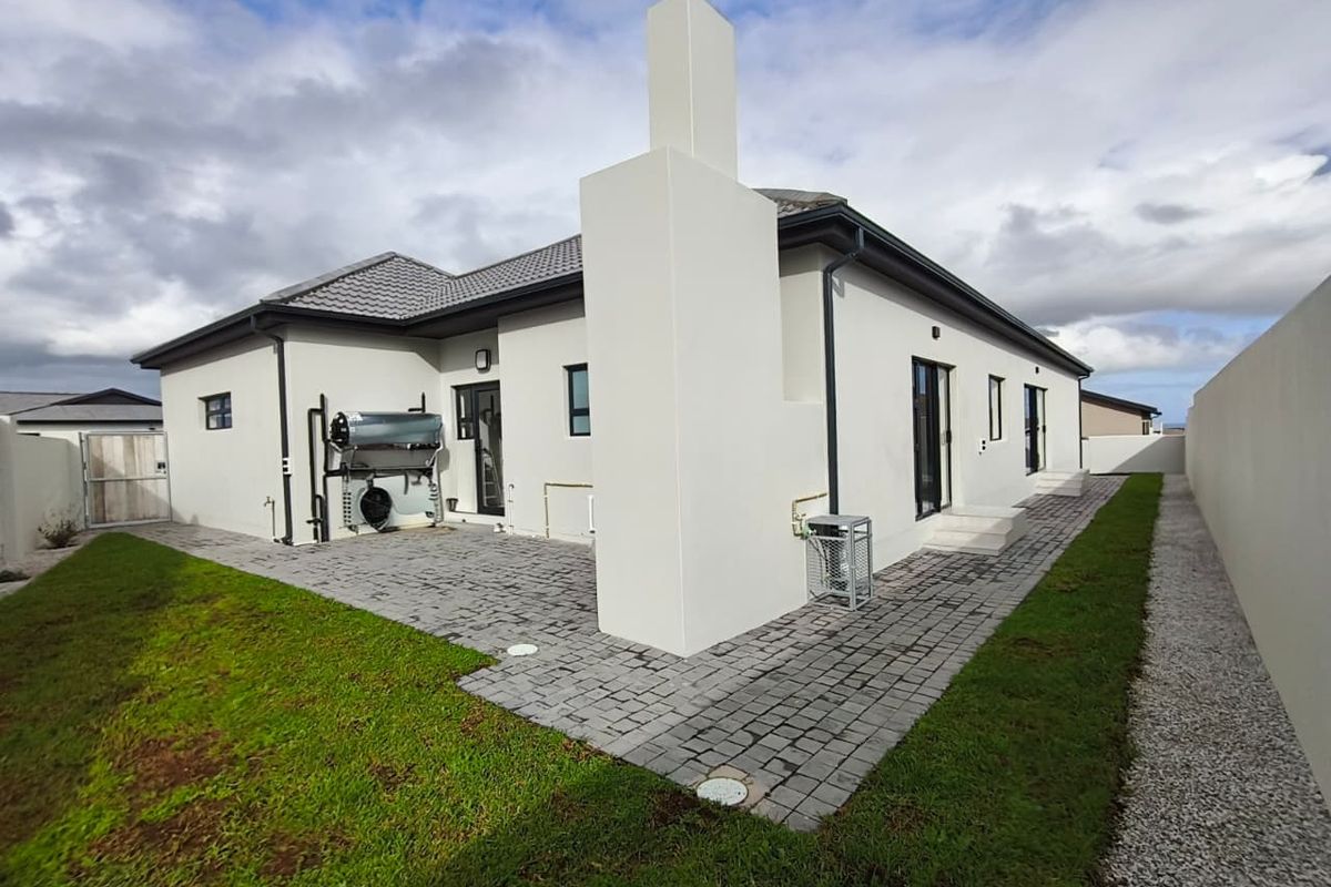 Rear view of the property featuring a paved patio area, solar water heating system, and a prominent chimney stack against a well-maintained exterior.
