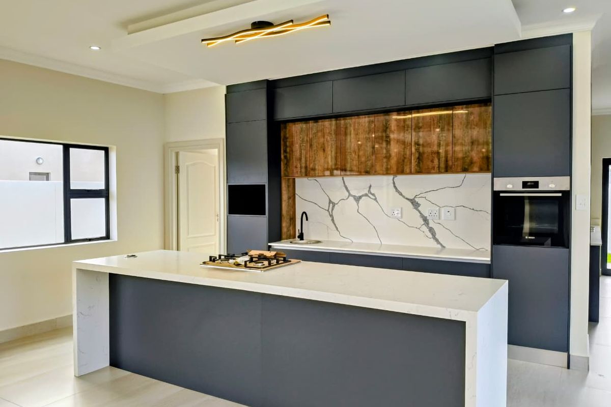 Modern kitchen featuring a large central island with quartz countertops, built-in oven, gas hob, and stylish dark cabinetry with wood-grain accents.