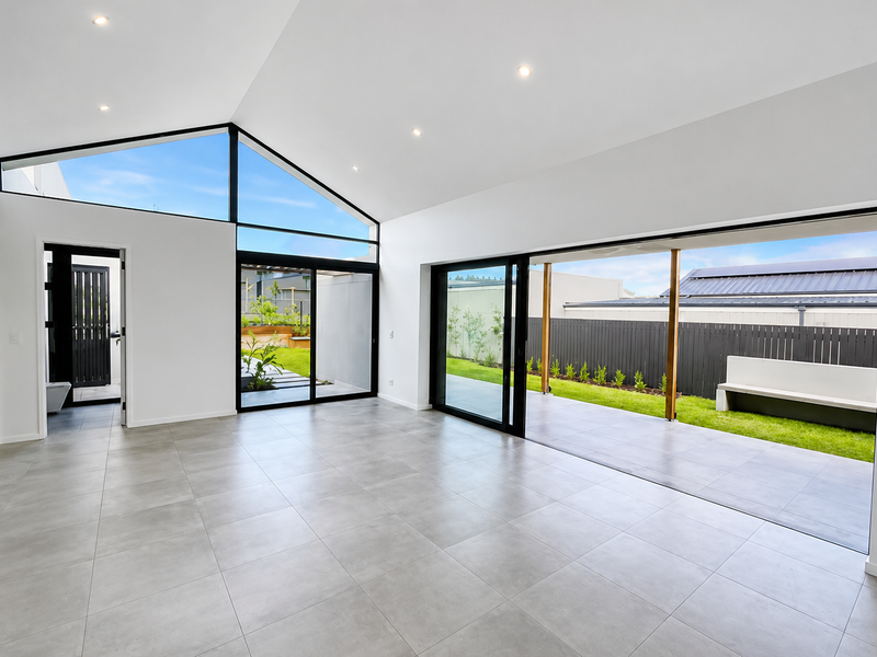 Spacious open-plan living area featuring vaulted ceilings, large format floor tiles, and expansive sliding glass doors opening onto a covered patio and garden.