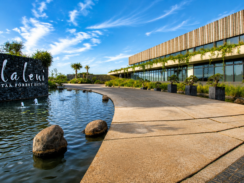 The entrance to Elaleni Coastal Forest Estate features a modern architectural facade, stone-clad signage, and a tranquil water feature along the paved driveway.