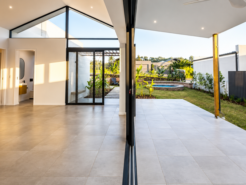 Spacious open-plan living area featuring vaulted ceilings, large sliding glass doors, and seamless transition to a covered patio and private garden with pool.