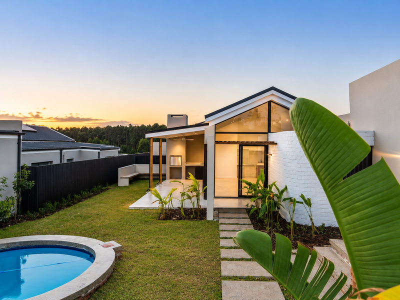 A beautifully landscaped rear garden featuring a modern swimming pool, a covered patio with a built-in braai, and contemporary architectural design.