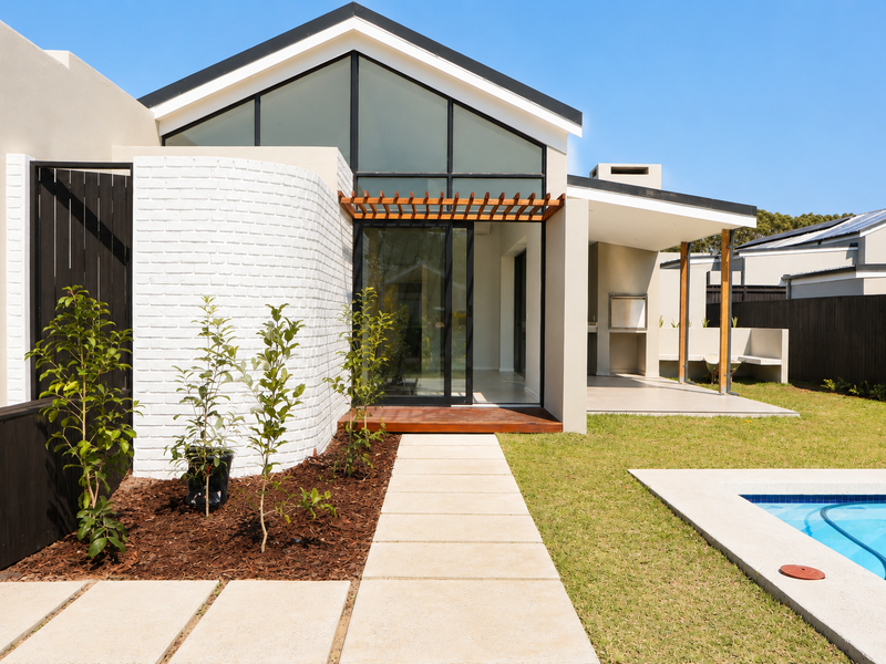 Modern rear exterior featuring a swimming pool, timber decking, a built-in braai area, and a striking white brick feature wall with large glass doors.