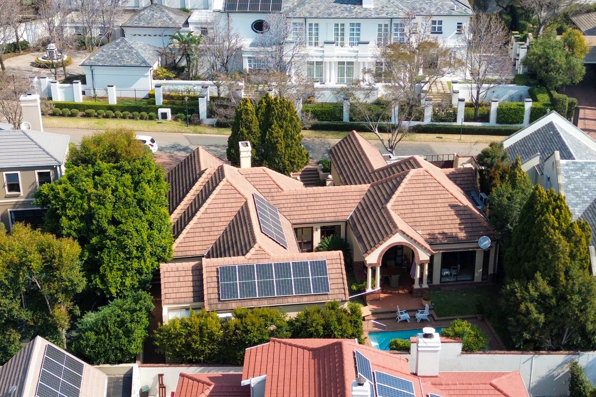 Aerial view of a residential property featuring a tiled roof with installed solar panels, a private swimming pool, and a paved patio area.