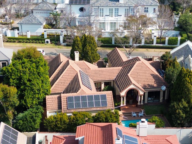 Aerial view of a residential property featuring a tiled roof with installed solar panels, a private swimming pool, and a paved patio area.