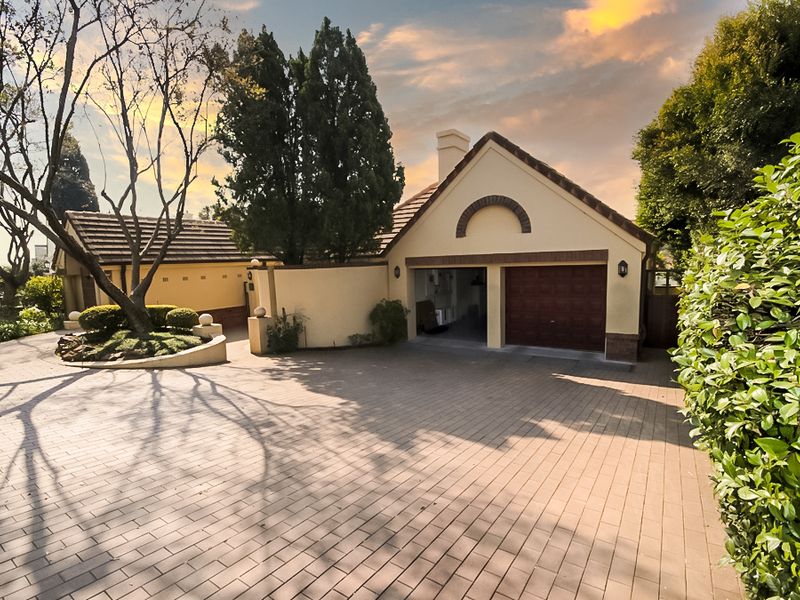 Front exterior view of the property featuring a paved driveway, double garage, and well-maintained landscaped garden area.