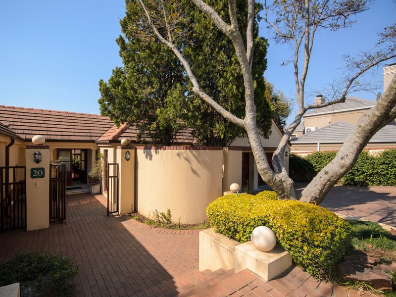 The front entrance features a brick-paved walkway leading to a private courtyard, complemented by a curved boundary wall and established landscaping.