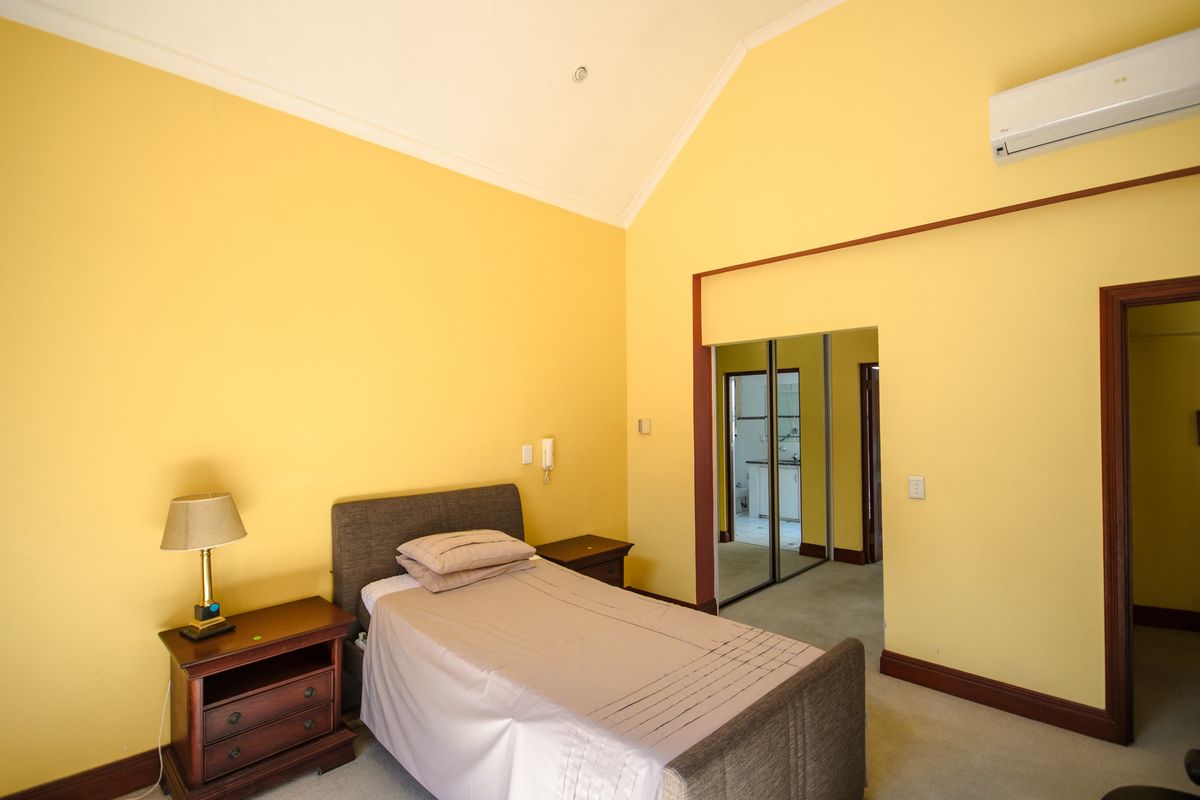 Spacious bedroom featuring a vaulted ceiling, carpeted flooring, a built-in sliding wardrobe, and a wall-mounted split-system air conditioning unit.