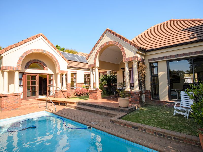 A well-maintained rear exterior featuring a swimming pool, brick-paved surround, and a covered patio area with architectural brick columns and tiled roofing.