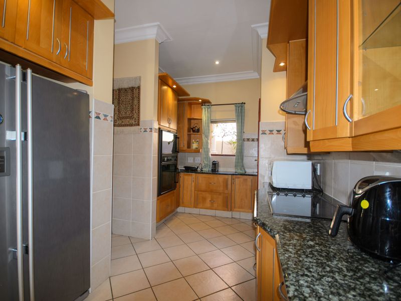 A functional kitchen featuring wooden cabinetry, granite countertops, built-in oven, extractor fan, and tiled flooring with a neutral backsplash.